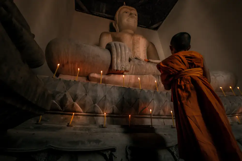 The Burning House parable from the Lotus Sutra. A novice pays homage to a large stone statue of the Buddha with burning candles